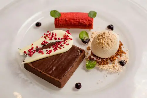 Dine | Exclusive Weddings & Events in Yorkshire | A Yorkshire wedding wouldnt be complete without this gourmet dessert platter featuring a chocolate brownie topped with white chocolate and red sprinkles. Delight in ice cream on crumbled biscuit and a red, cylindrical mousse garnished with green leaves and small berries. Perfect for any event!.